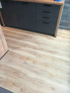 Kompletně položená světlá laminátová podlaha Krono Original o síle 6 mm v uličce mezi tmavými kuchyňskými bloky.