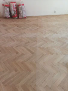 Srovnání vybroušeného dřeva a plochy po aplikaci základního laku – precizní práce, kterou odvádějí mistři podlaháři.