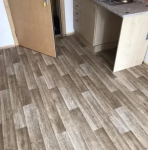 Pokládka PVC Ambient v dekoru tmavého dřeva v kuchyni a přechod u dveří.