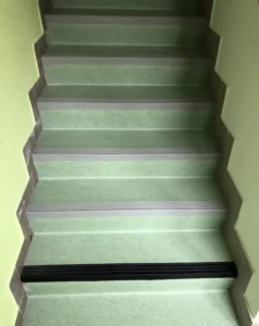 Detailní pohled na schodiště s PVC Gefloor, hliníkovými hranami a precizně vyřezaným bočním soklem