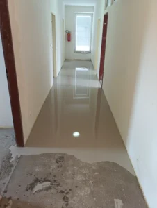 Rekonstrukce podlahy v Ostravě - kontrast mezi původním betonem a novou samonivelační stěrkou v chodbě.