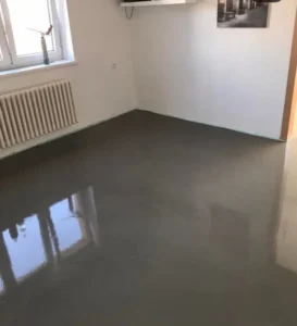 Rozlitá samonivelační stěrka v místnosti s odrazem oken, detail u radiátoru.